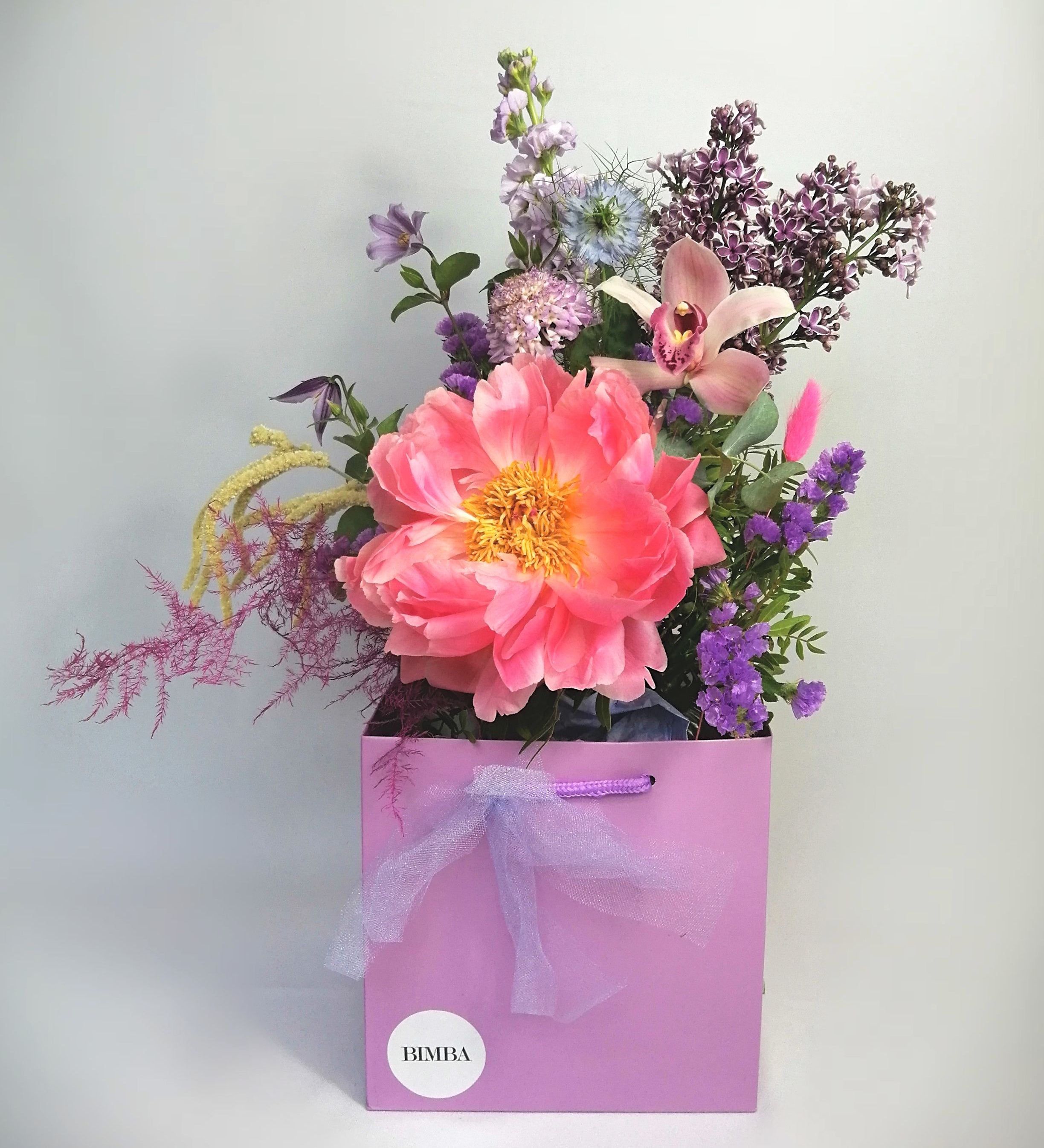 CELINE BOUQUET Beautiful flower arrangement, featuring a mix of summery flowers in lovely violet, blue and coral tones, like orchids, delphinium, French Clematis, Limonium, Sweet scented eucalyptus and colourful asparagus fern accompanied of our star 'Peony Coral Charm' perfect to brightening up the day. By Bimba Floral Studio.