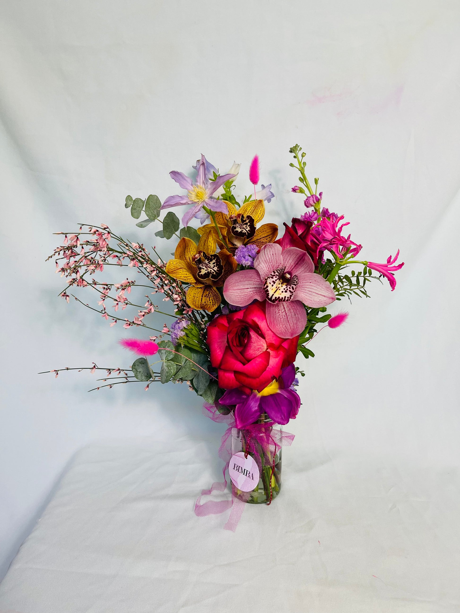 CHA- CHA- CHA Bouquet Beautiful flower arrangement featuring blooms in reds, purples, pinks and with yellow accents.  Like roses, luxury orchids, sweet scented stock, hot pink asparagus, playful bunny tails and eucalyptus. Arriving with a glass vase ready to enjoy.
