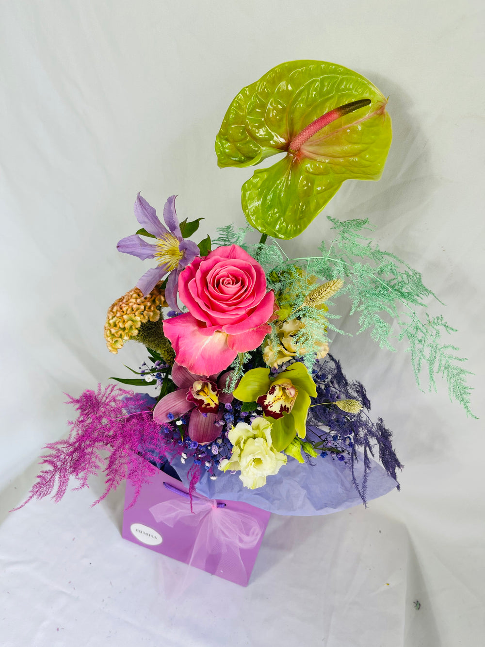 Lucky bouquet  is a blissful flower arrangement featuring Caribbean Anthurium ,french clematis, sweet scented rose, exotic orchids, rainbow gypsophila, blush lisianthus, agapanthus, stunning celosia and painted asparagus fern in bright colours. By Bimba Floral Studio.