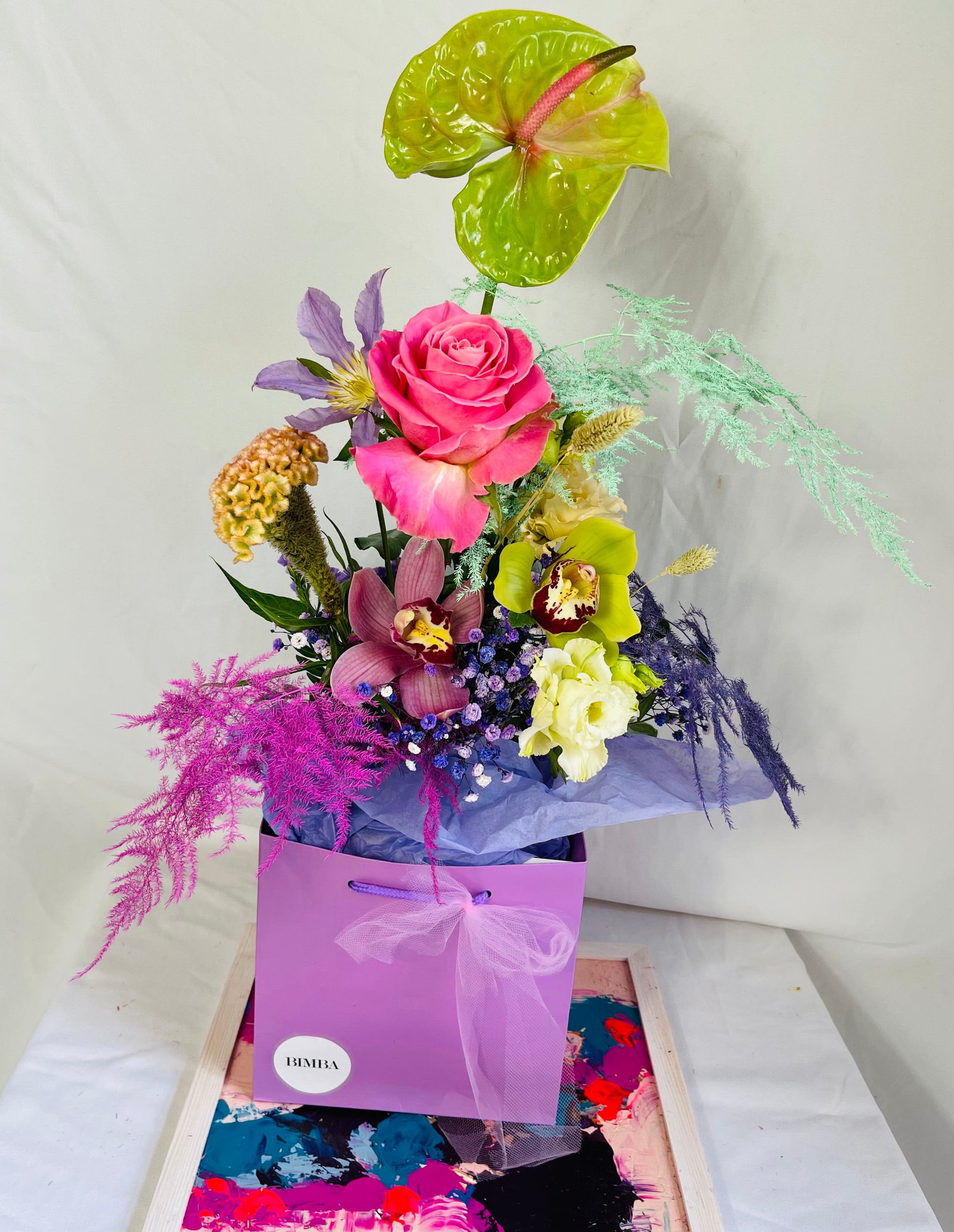 Lucky bouquet  is a blissful flower arrangement featuring Caribbean Anthurium ,french clematis, sweet scented rose, exotic orchids, rainbow gypsophila, blush lisianthus, agapanthus, stunning celosia and painted asparagus fern in bright colours. By Bimba Floral Studio.