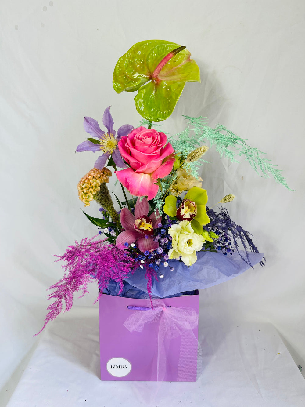 Lucky bouquet  is a blissful flower arrangement featuring Caribbean Anthurium ,french clematis, sweet scented rose, exotic orchids, rainbow gypsophila, blush lisianthus, agapanthus, stunning celosia and painted asparagus fern in bright colours. By Bimba Floral Studio.