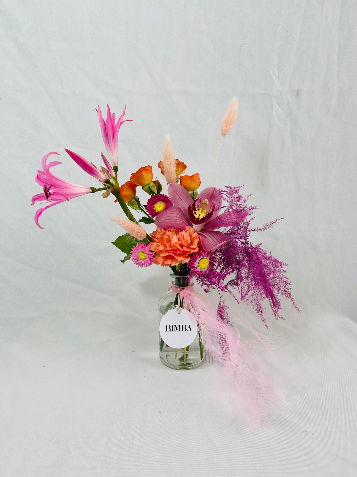 Full of grace mini floral arrangement, in hues of fuchsia and orange tones featuring luxury orchids, eye-catching nerine or french Clematis, sweet scented  mini blooms, timeless carnation, dried conserved acroclinium or camomille flower, asparagus fern and bunny tails.